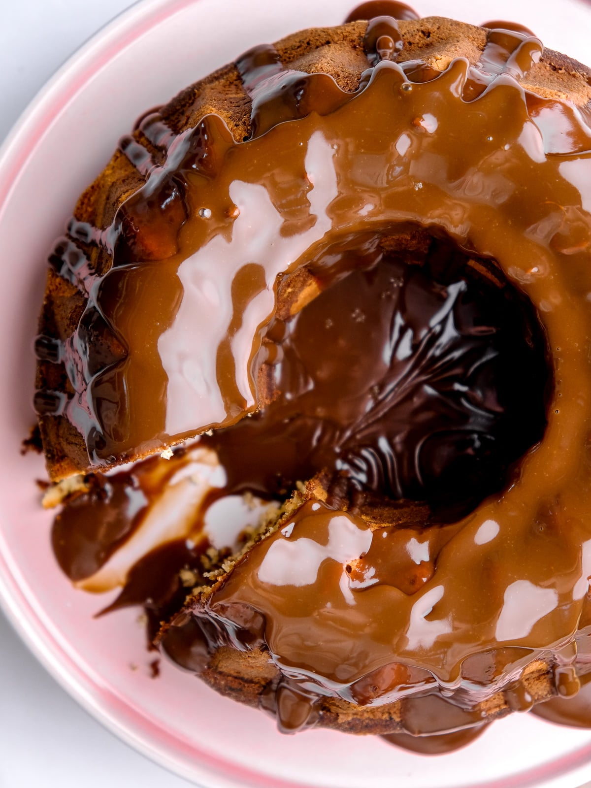 Image shows the Marble Bundt Cake from above, a slice has been cut. You can see the shiny chocolate sauce covering the cake.