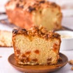 A slice of the loaf cake in shown in front of the whole loaf. You can see the crunchy topping.