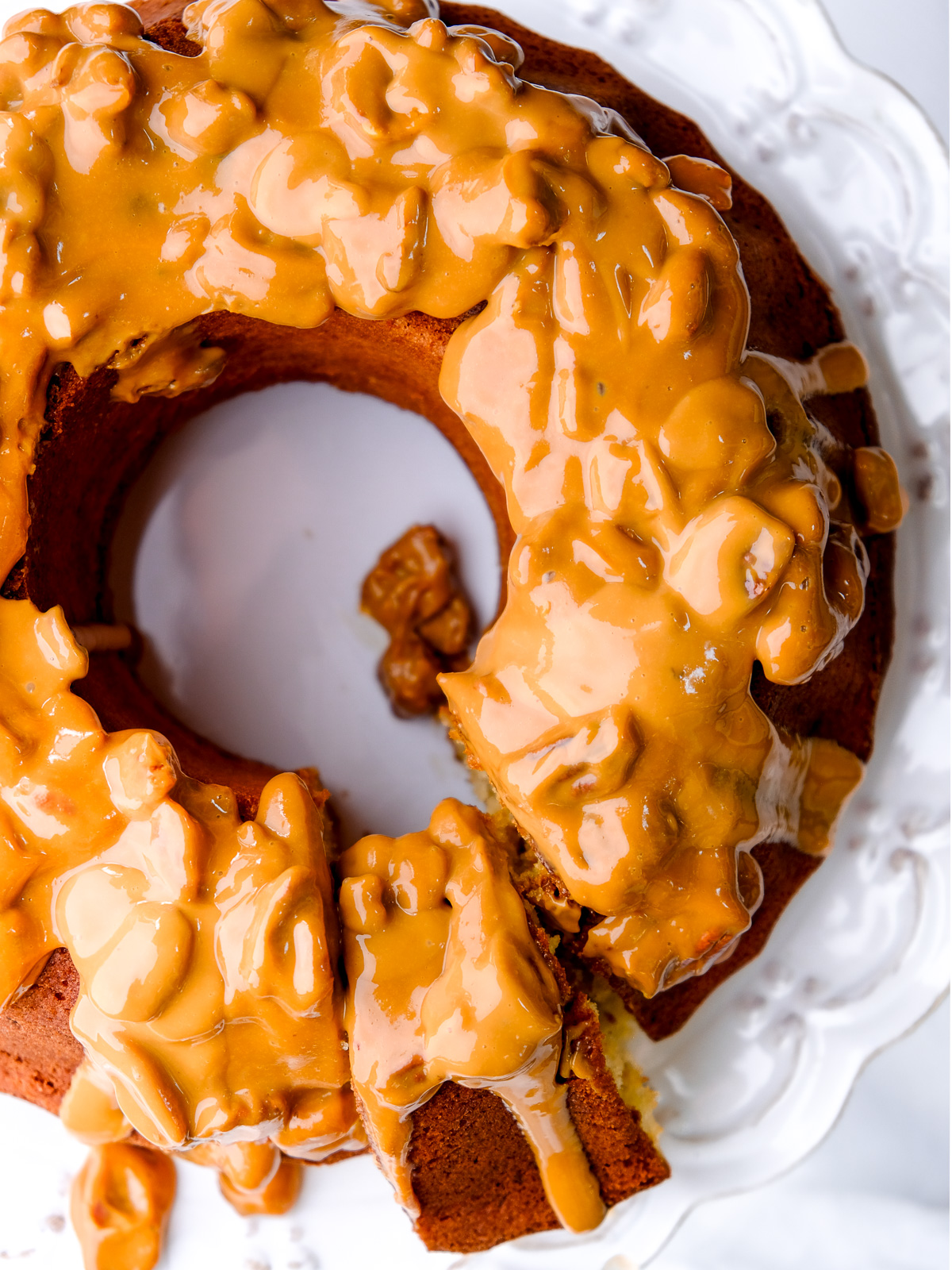 Image shows Banana Bundt Cake with Sour Cream from above, a slice has been cut. You can also see the thick caramel sauce dripping off the side of the cake.