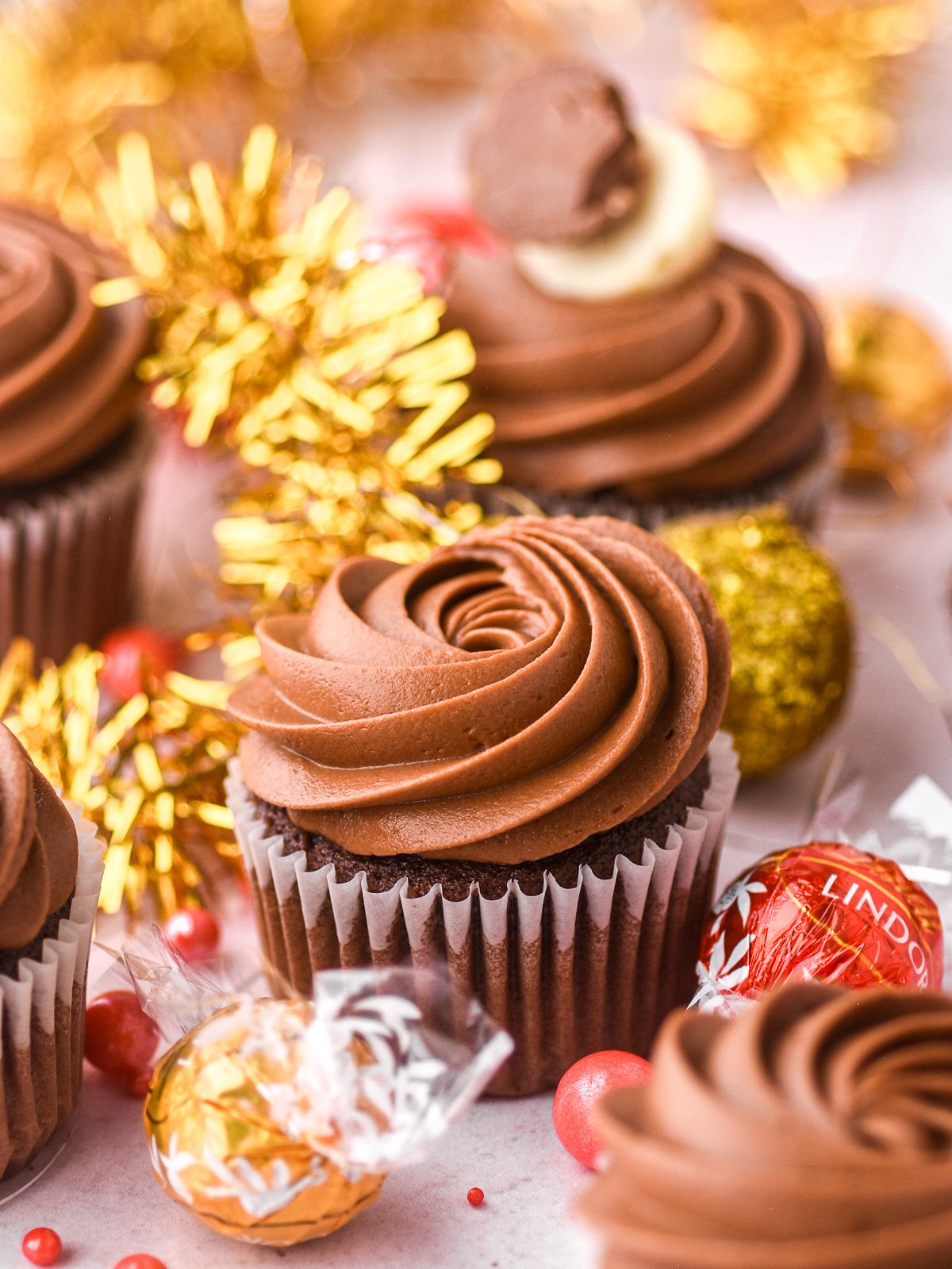 Frosted cupcake with gold Christmas decorations in the background.