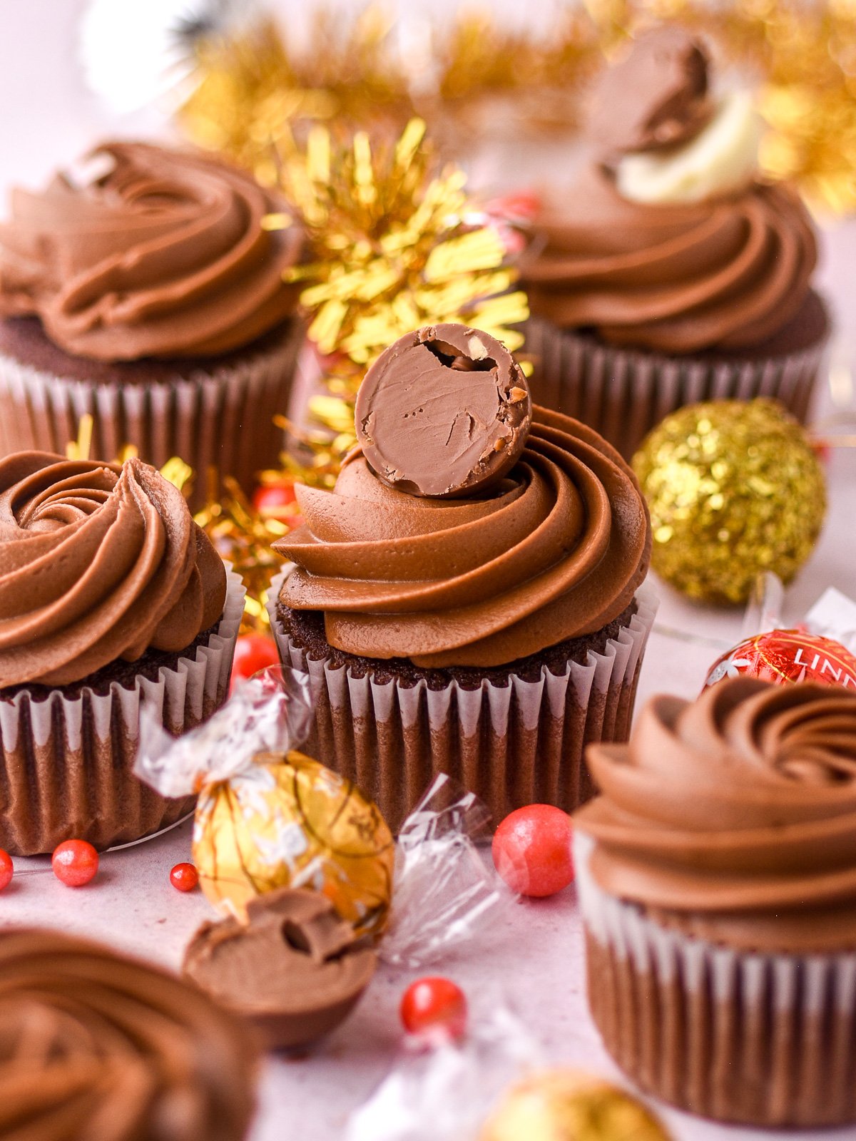 Decorated cupcakes shown next to Christmas tinsel and Lindor balls in their wrappers.