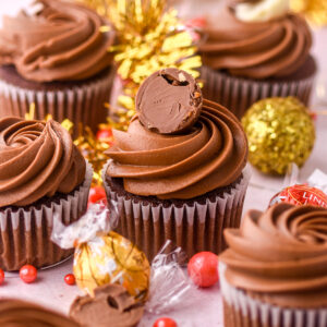 Lindt Chocolate Stuffed cupcakes shown decorated on a kitchen counter next to tinsel and Christmas decorations.