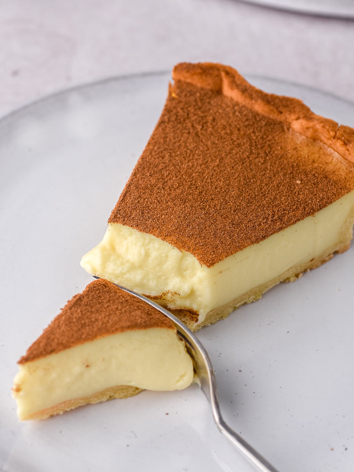 Up close image of a slice of milktart with a fork through it. You can see the creamy texture of the cinnamon custard filling.