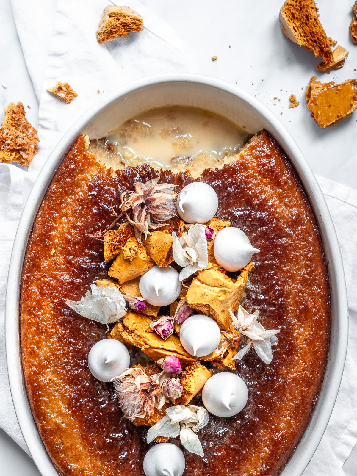 Overhead image of a South African malva pudding which has been baked in an oval dish and decorated with mini meringues.