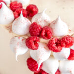 Mini meringues shown decorating a cake, they have been stuck onto the cake next to raspberries.
