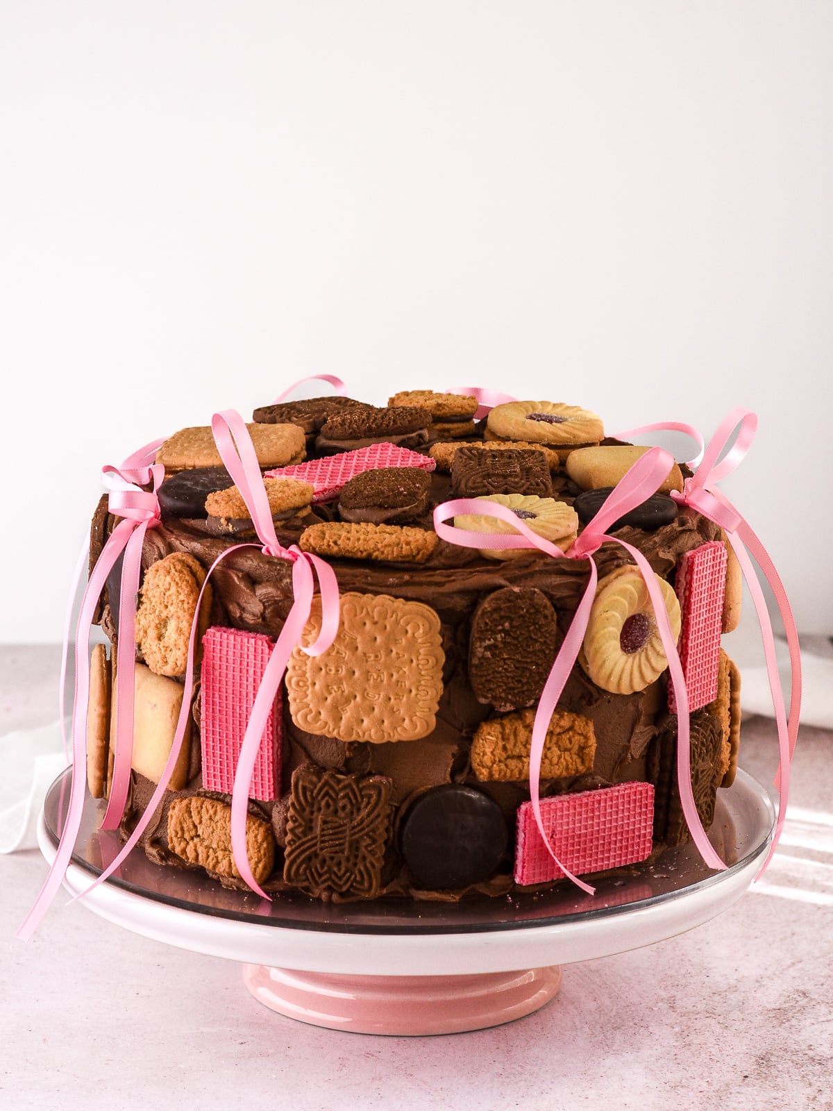 Image shows chocolate cake covered in chocolate frosting and decorated with pink ribbons and different shaped cookies.