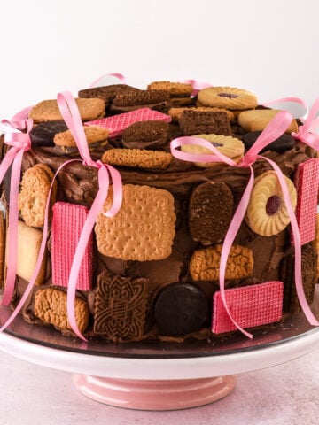 Image shows full on a pink cake stand. It's decorated with ink ribbons and an assortment of biscuits.
