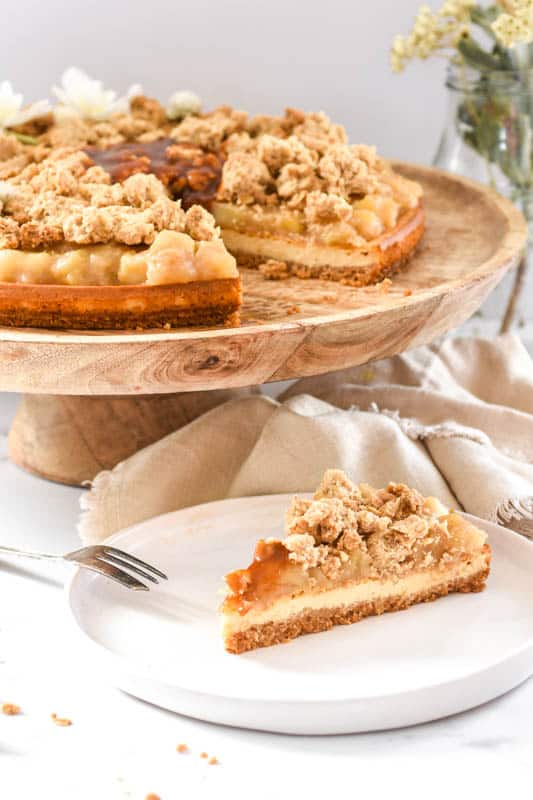 Apple Crumble Cheesecake shown on a cake stand with a slice missing 