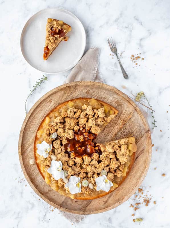 Apple Crumble Cheesecake shown from above with a slice missing and on a plate 