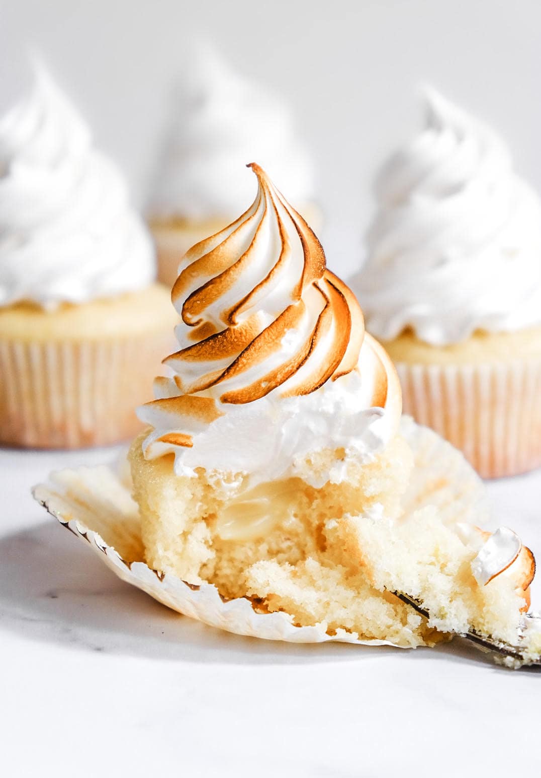 Lemon Meringue Cupcake shown with a spoonful missing so that you can see the lemon filling inside.