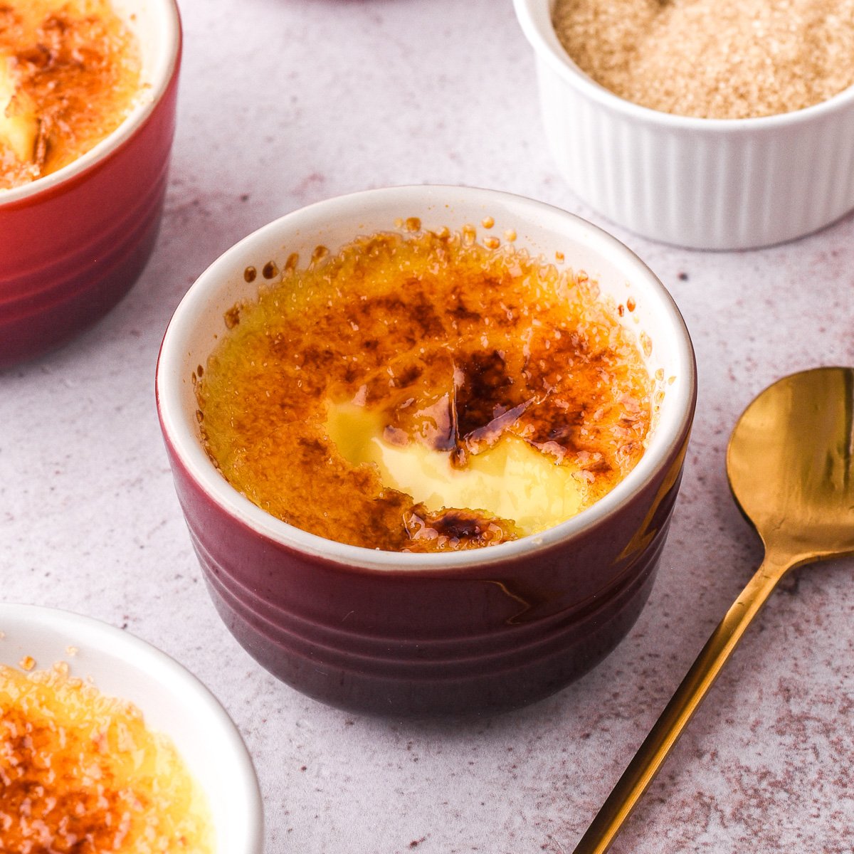 Image shows the crème brûlée with the sugar crust that has been cracked next to a spoon.