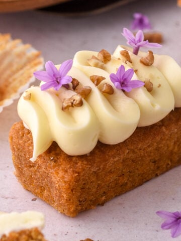 Mini carrot cake loaf cake shown on a counter top decorated with piped cream cheese frosting and chopped walnuts.