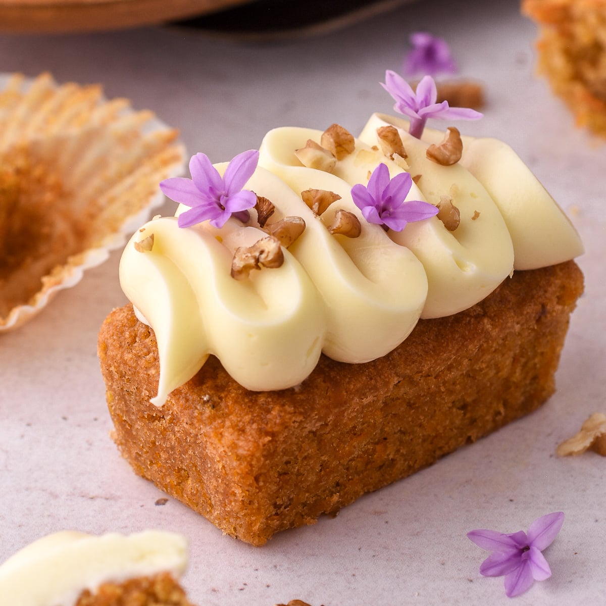 Mini carrot cake loaf cake shown on a counter top decorated with piped cream cheese frosting and chopped walnuts.