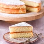 A slice od cake shown on a plate set in front of the whole cake. You can se the layer of jam in between the cake layers.