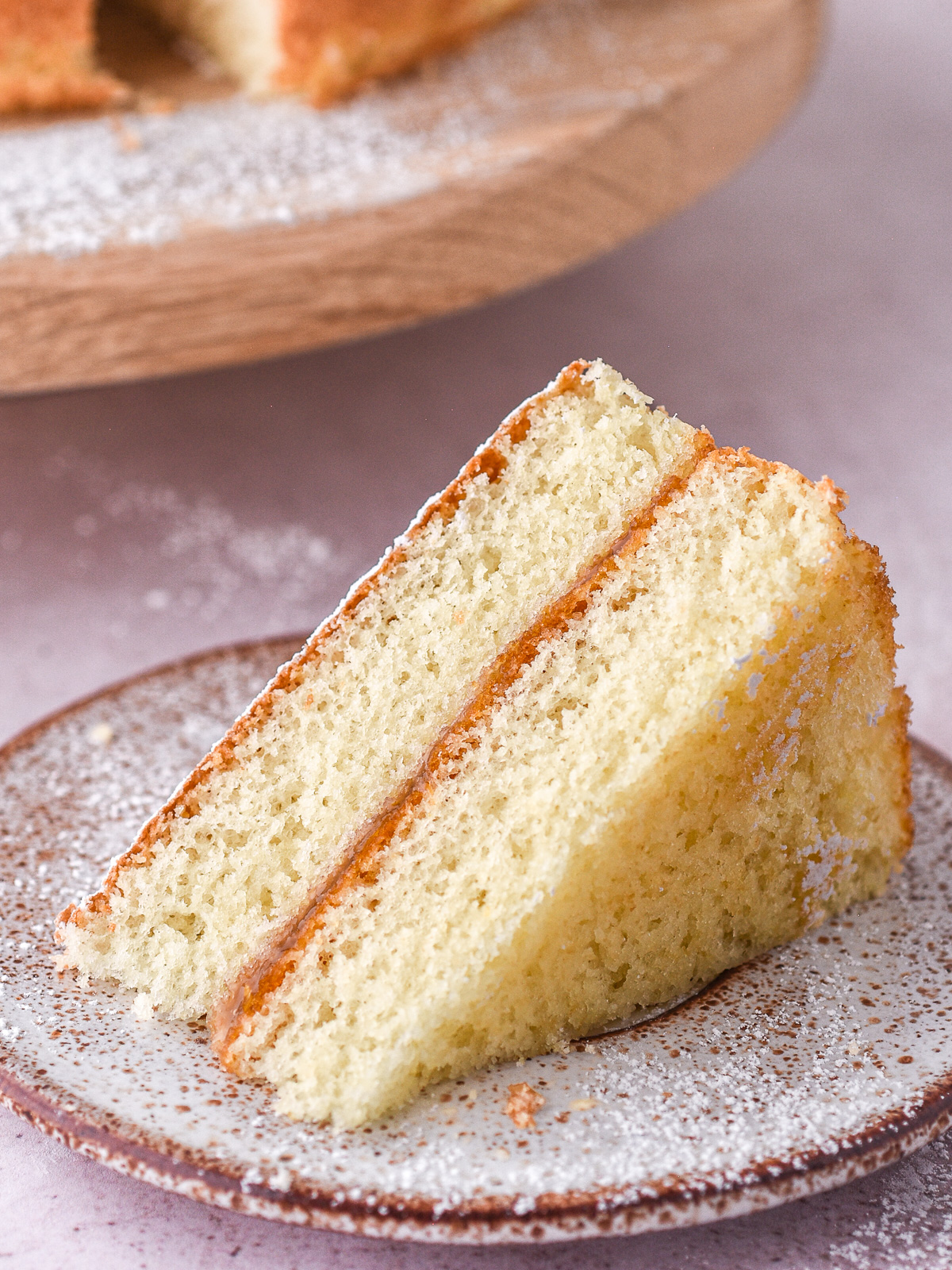 Image shows a slice of hot milk sponge cake, you can see the even layers of cake sandwiched together with a layer of apricot jam.