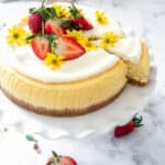The Best Lemon Cheesecake with White Chocolate Cream, shown on a serving plate with strawberries