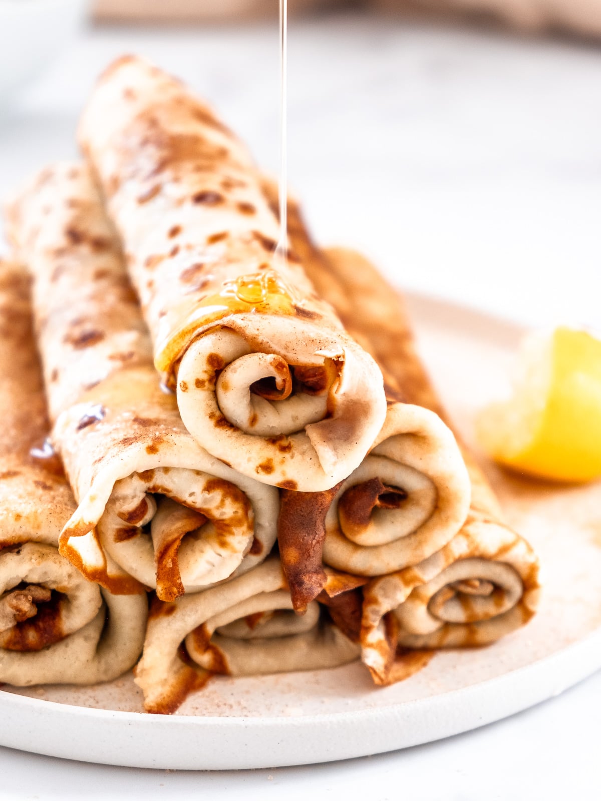 Image shows a stack of cinnamon sugar South African pancakes, they have been rolled up.