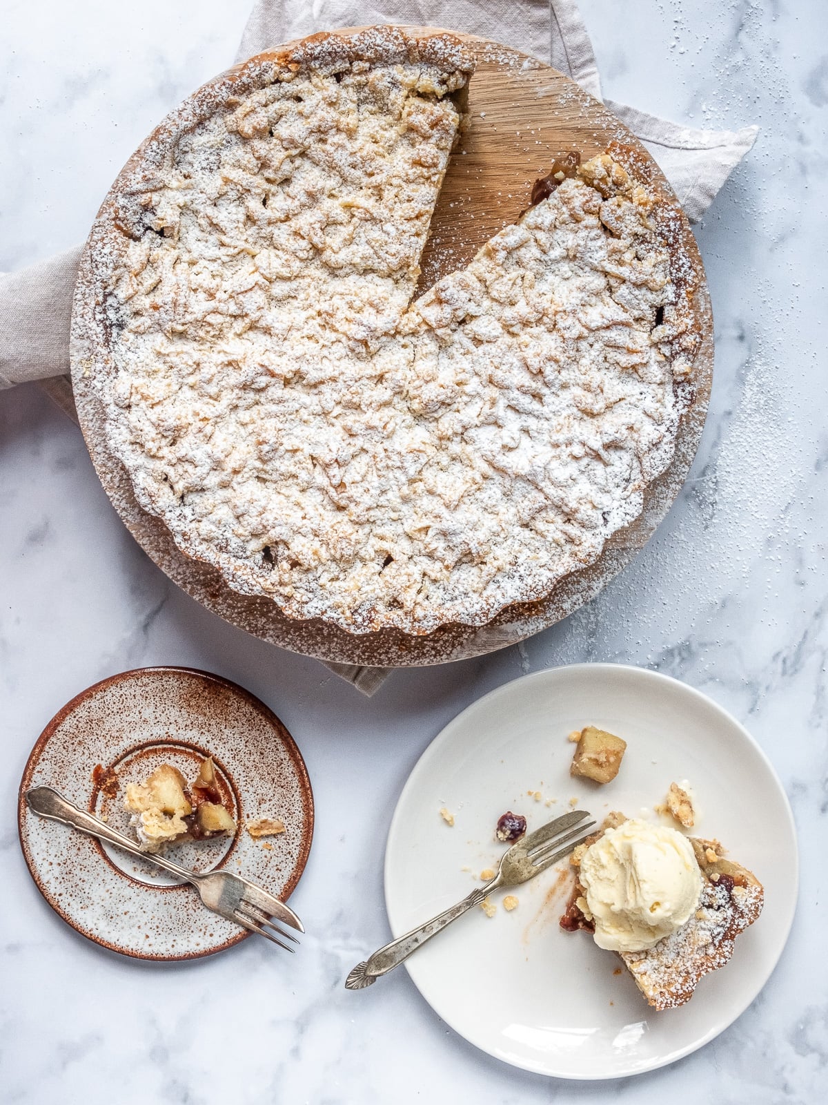 Apple and Cranberry Crumble Tart dusted with icing sugar shown from above with a slice missing.