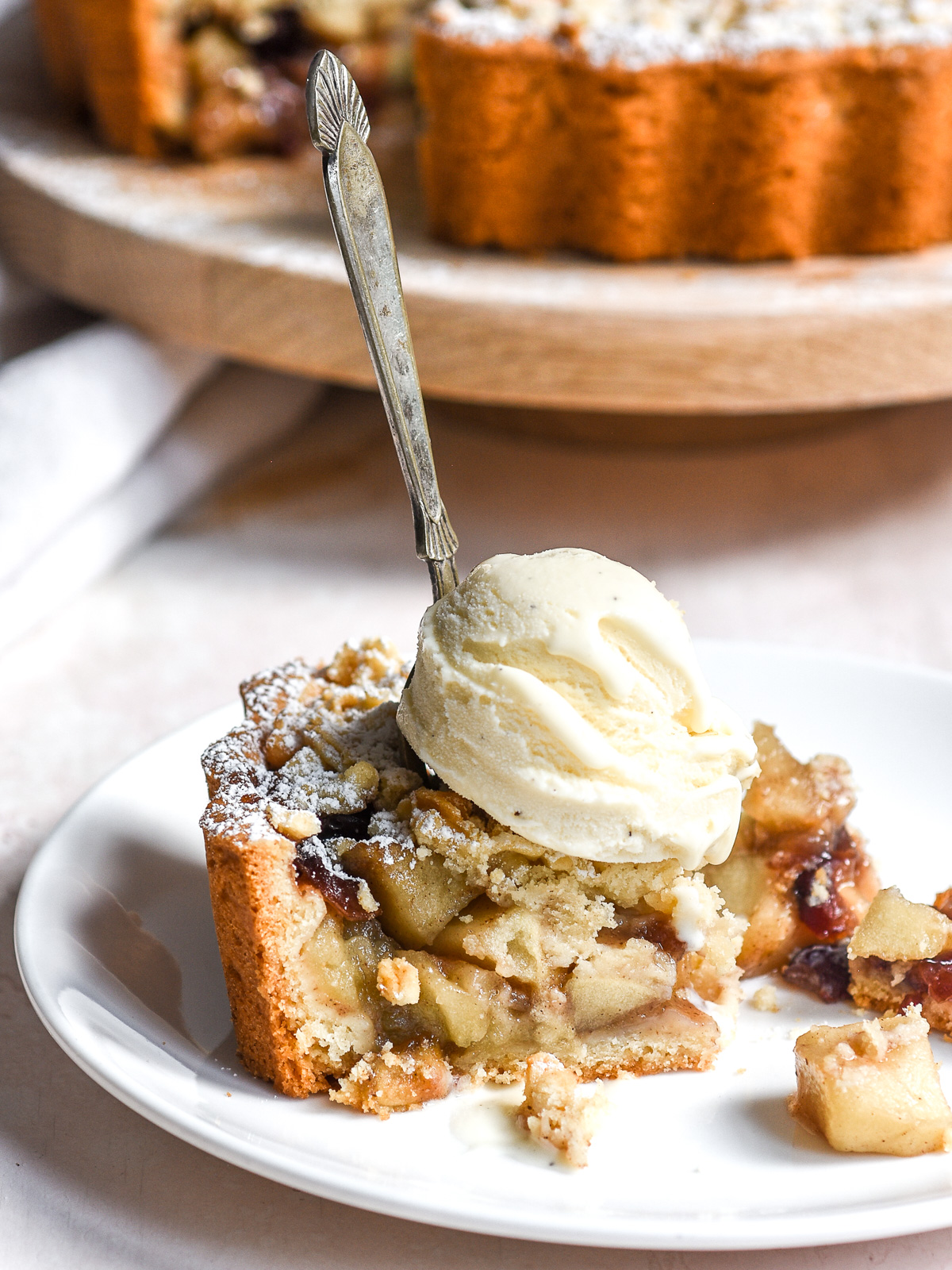 A slice of Apple and Cranberry Crumble Tart on a plate with a scoop of ice cream on top and a fork sticking through the slice.