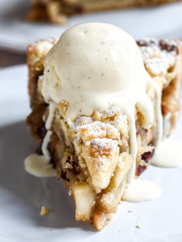 Slice of Apple and Cranberry Crumble Tart shown with a dripping scoop of ice cream on the top.
