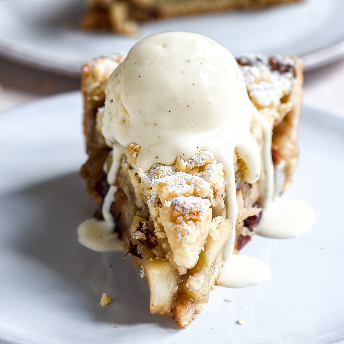 Slice of Apple and Cranberry Crumble Tart shown with a dripping scoop of ice cream on the top.