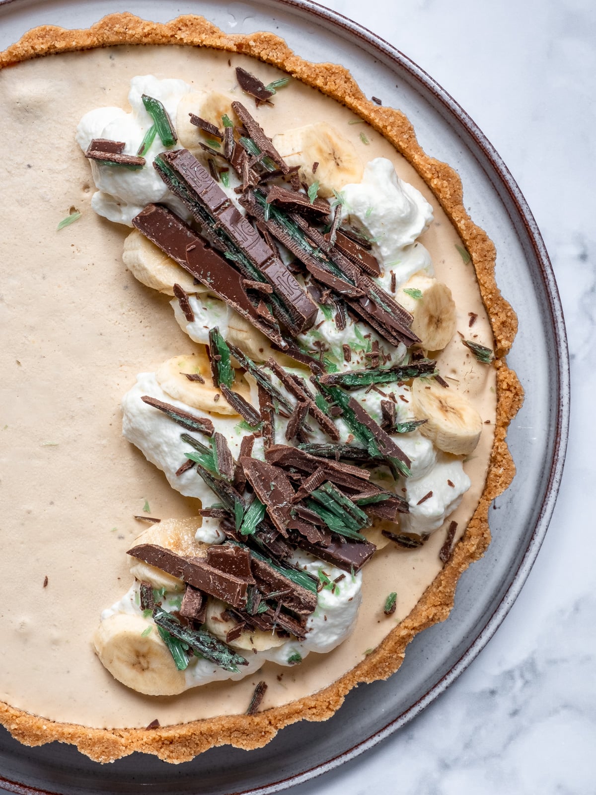 Caramel peppermint crisp tart shown from above. It has been decorated with whipped cream, sliced bananas, and chopped Nestle peppermint crisp pieces.
