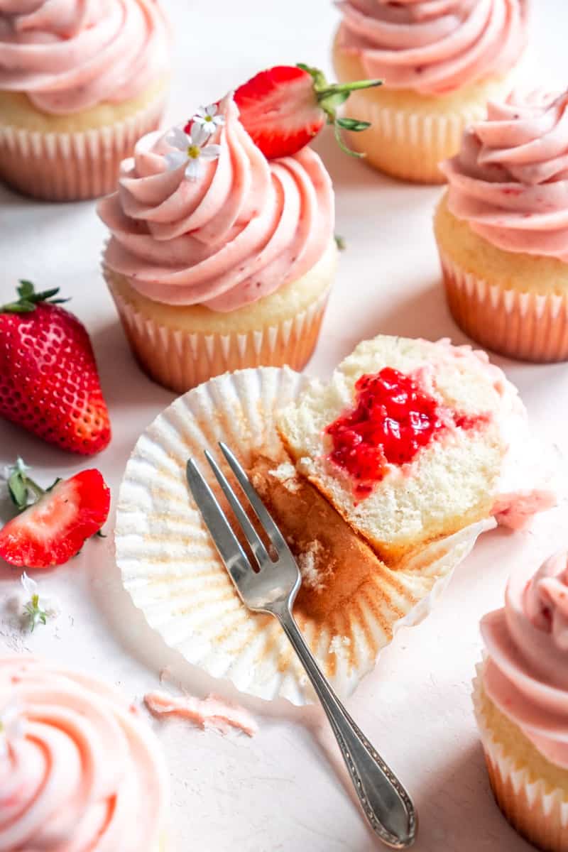 Strawberry Filled Cupcakes shown on a kitchen counter, once has been sliced open to see the strawberry center.
