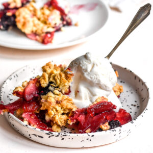 Apple and Blackberry Crumble shown on a plate with a scoop of vanilla ice cream.