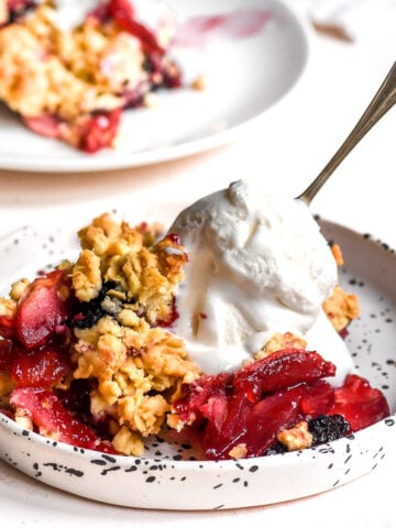 Apple and Blackberry Crumble shown on a plate with a scoop of vanilla ice cream.