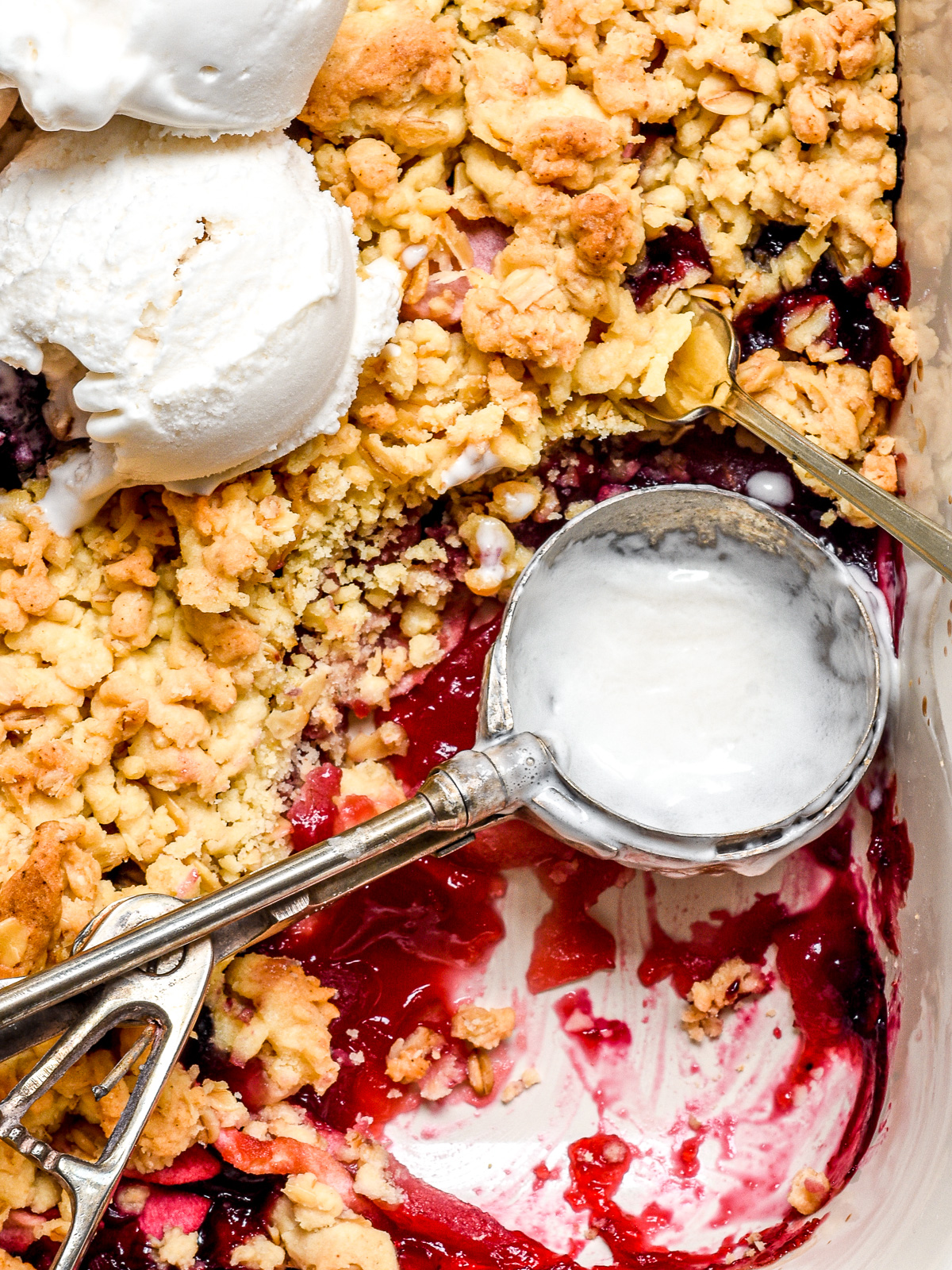 Apple and Blackberry Crumble shown from above in an oven dish with a scoop of ice cream.