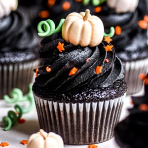 Black Velvet Halloween Cupcakes shown decorated with black buttercream frosting and edible mini pumpkins and orange stars.