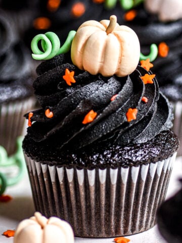 Black Velvet Halloween Cupcakes shown decorated with black buttercream frosting and edible mini pumpkins and orange stars.