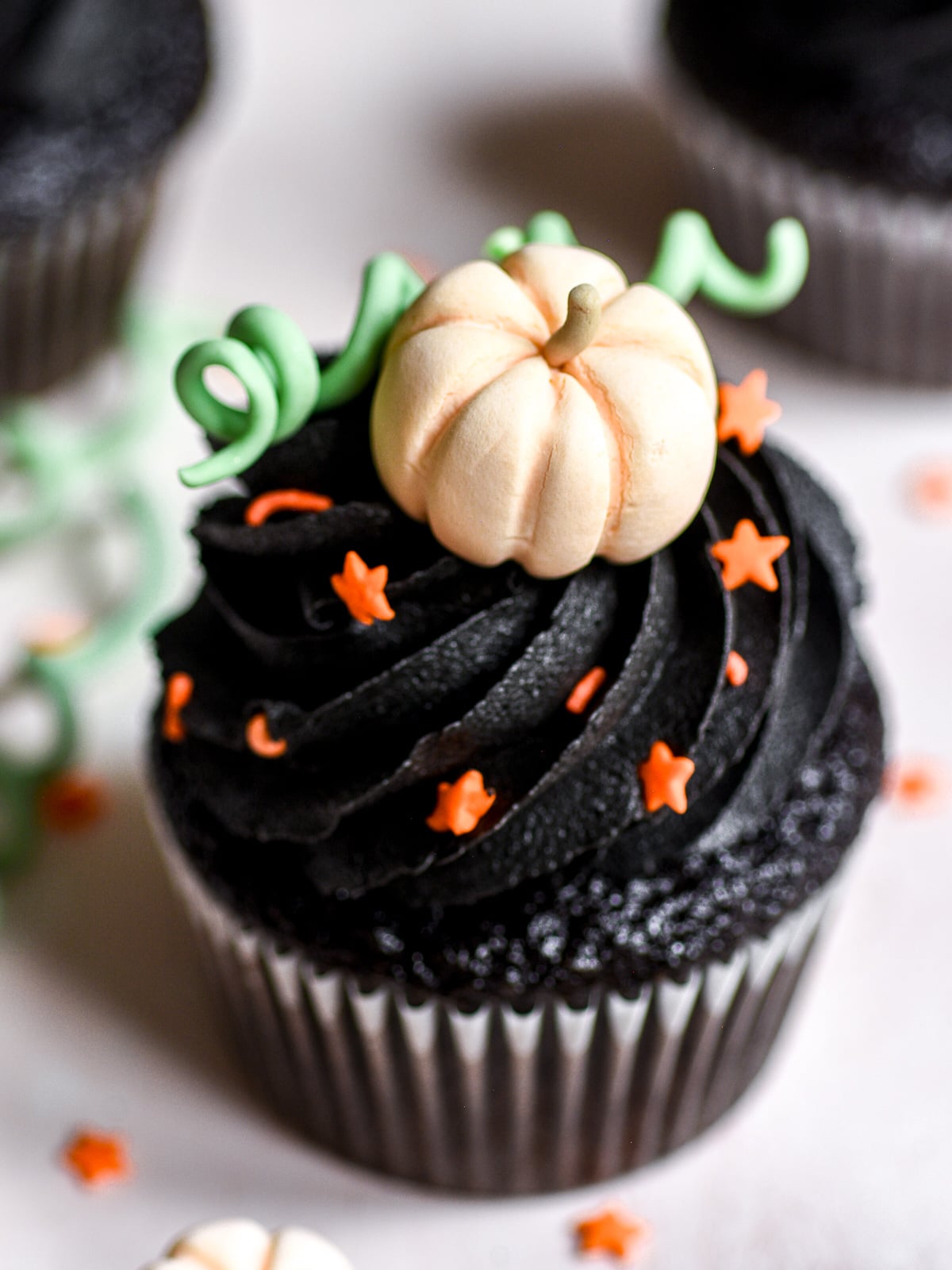 image shows Black Velvet Halloween Cupcakes with Black Buttercream Frosting decorated with homemade edible fondant pumpkins.