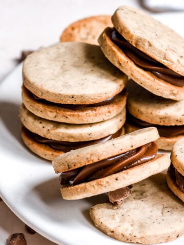 Coffee and Chocolate Ganache Sandwich Cookies shown on a white plate. You can see the shiny chocolate filling.
