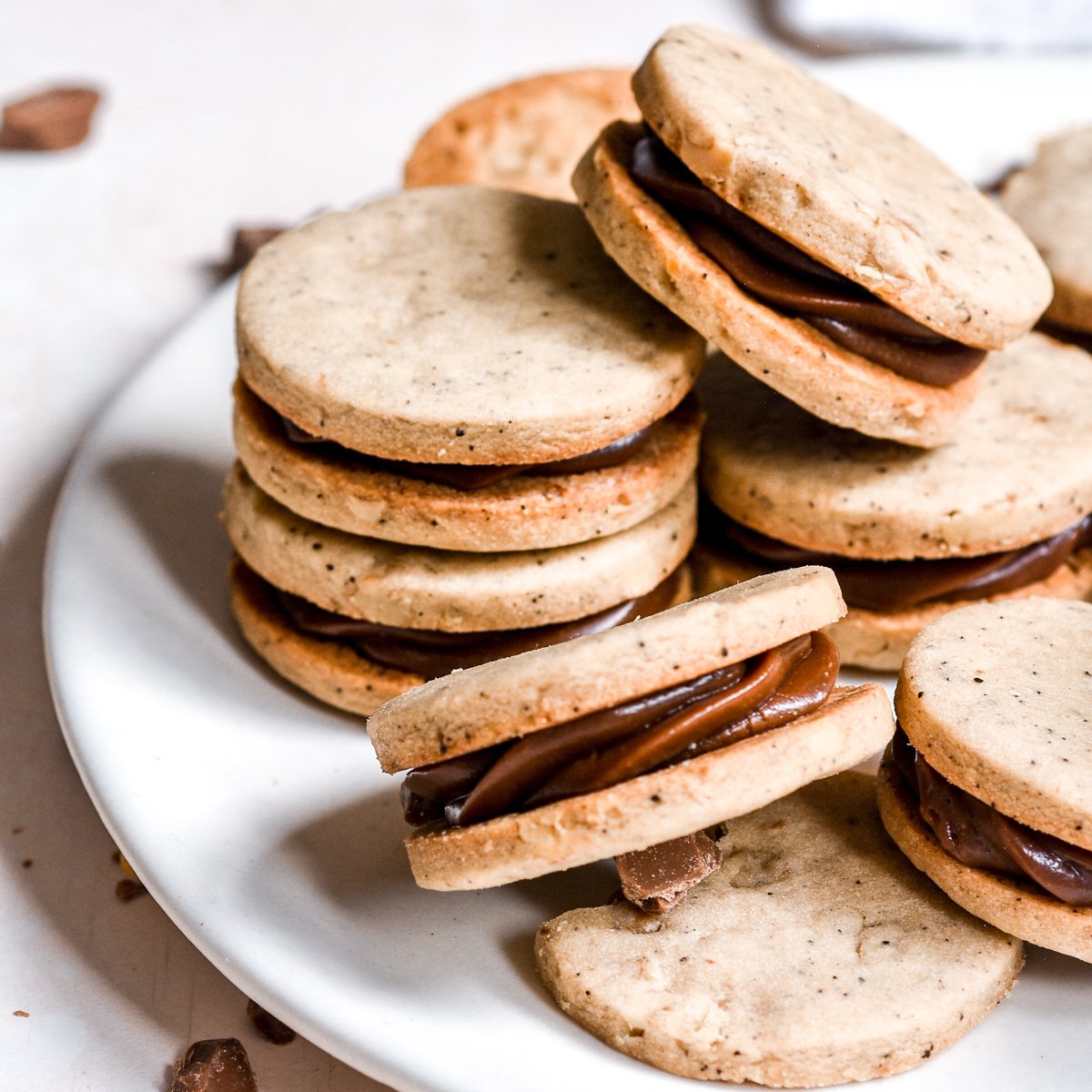 Coffee and Chocolate Ganache Sandwich Cookies shown on a white plate. You can see the shiny chocolate filling.