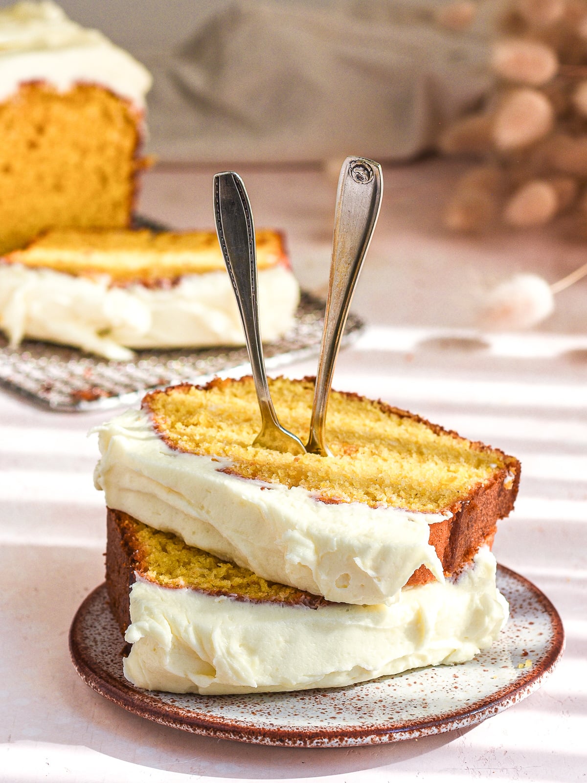 Two thick slices of pumpkin bread with cream cheese frosting shown on a small plate with two forks sticking out the top of the slices.