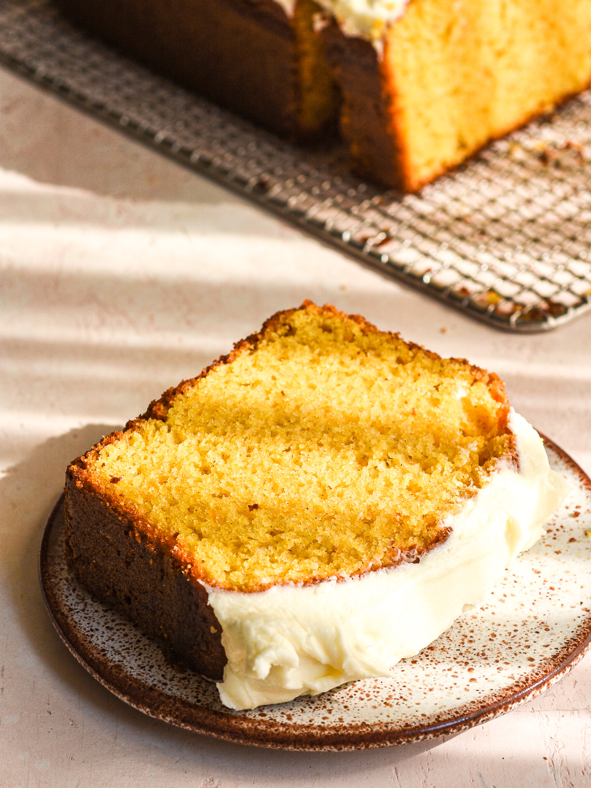 The perfect slice of pumpkin bread with cream cheese frosting shown on a small plate.