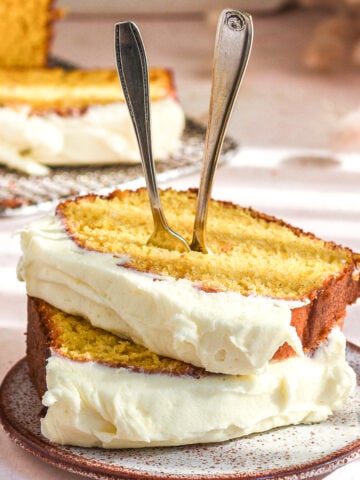 Two slices of pumpkin bread with cream cheese frosting shown on a small cake plate. Two forks are sticking out the the top of the slices.