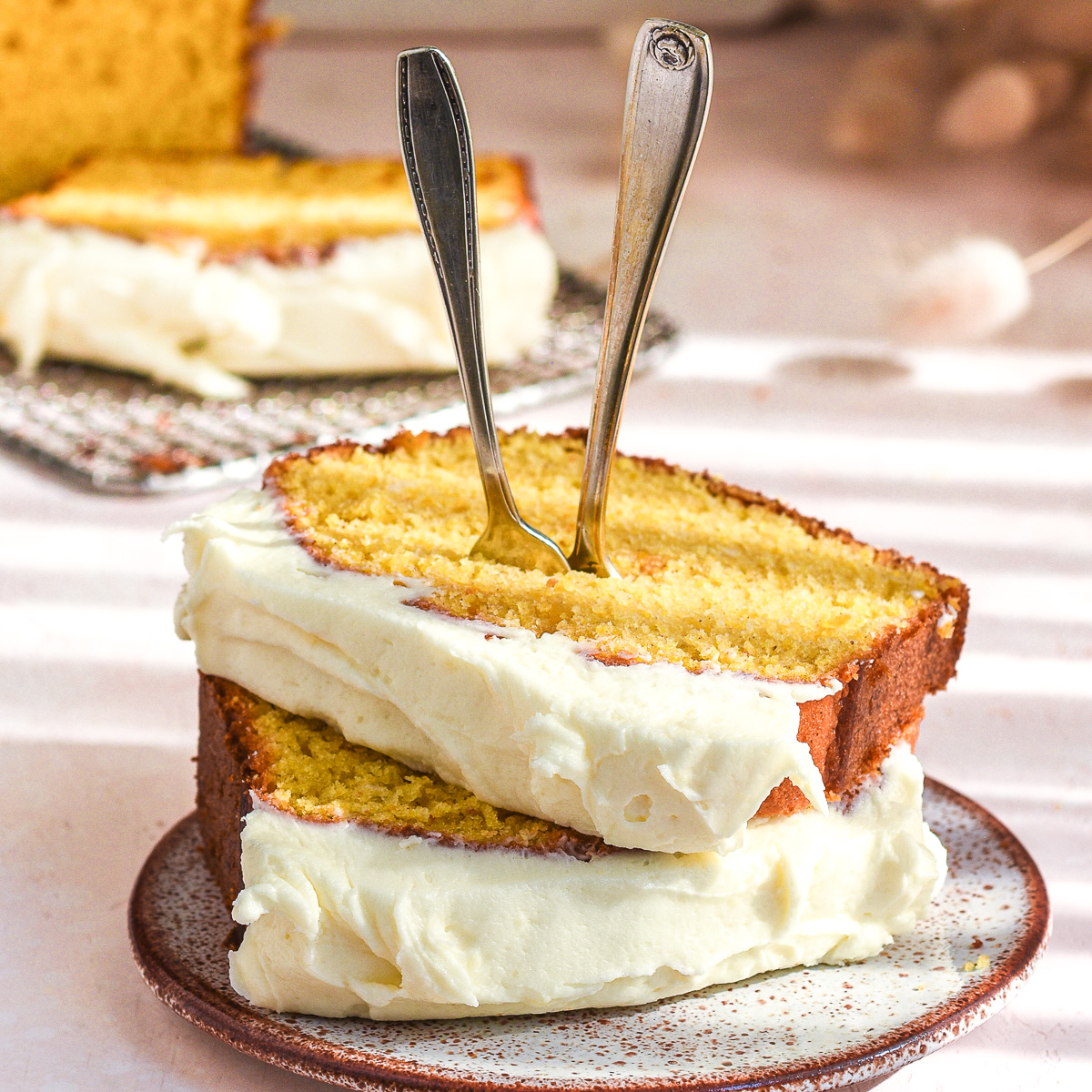 Two slices of pumpkin bread with cream cheese frosting shown on a small cake plate. Two forks are sticking out the the top of the slices.