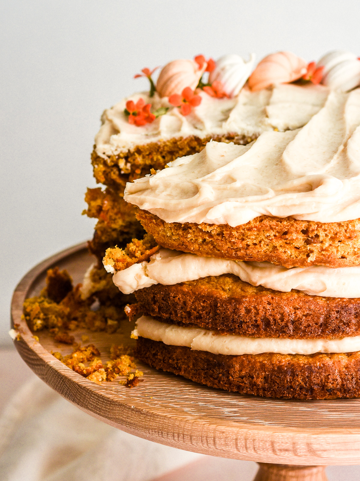 Pumpkin Carrot Cake with brown sugar cream cheese frosting shown on a wooden cake stand with a slice missing.