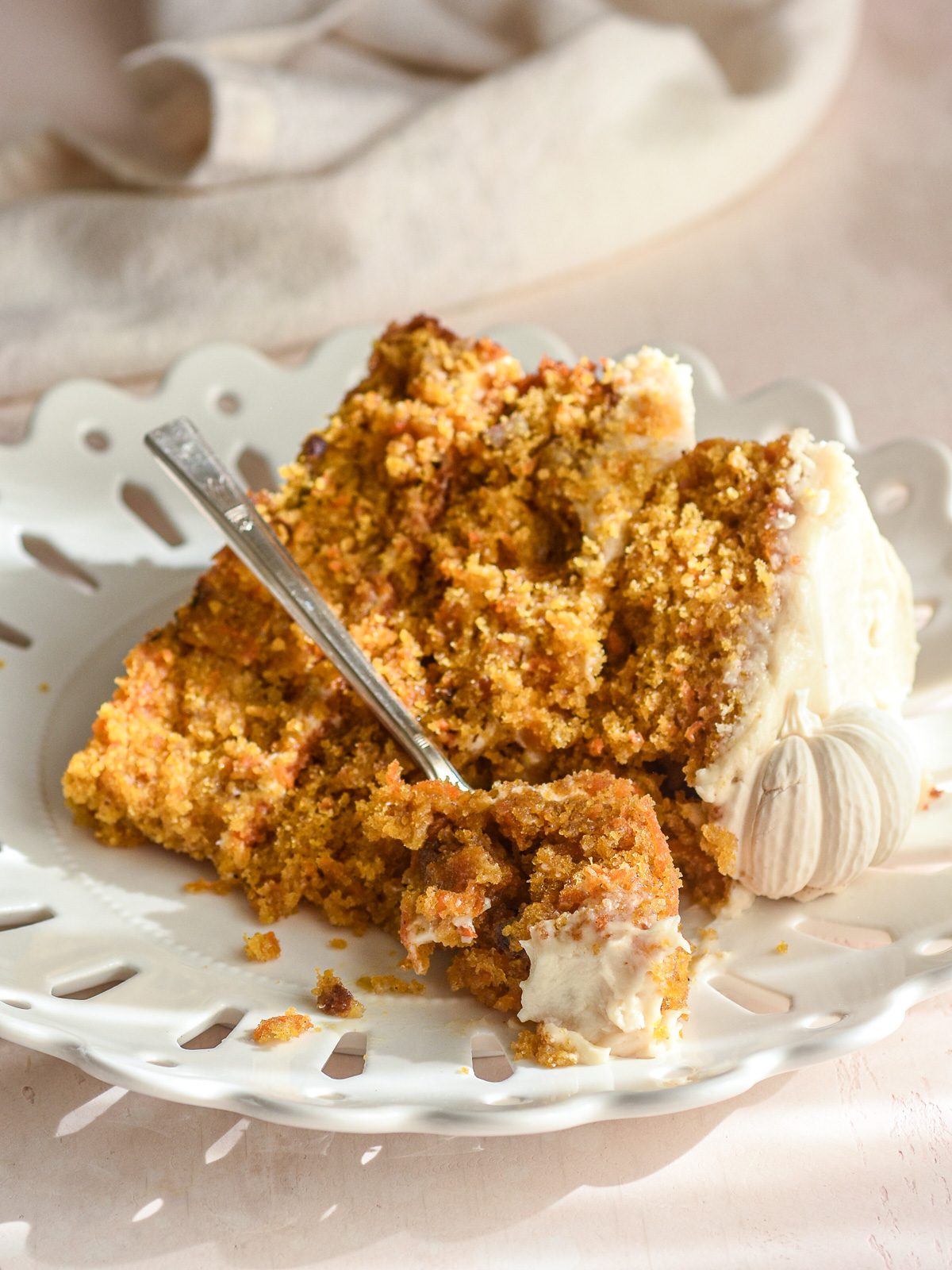 A slice of pumpkin carrot cake decorated with brown sugar cream cheese frosting and edible pumpkins shown on a small plate.