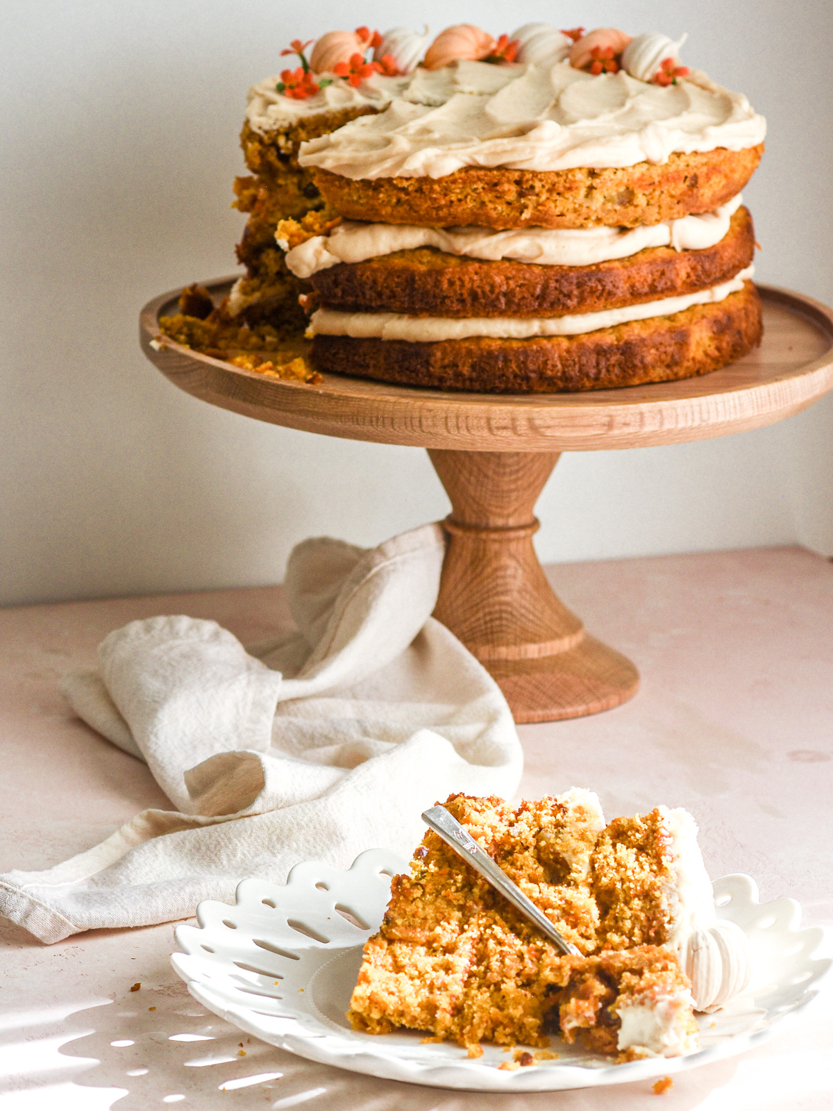 Pumpkin Carrot Cake on a cake stand with a slice on a plate shown in front of the cake stand.