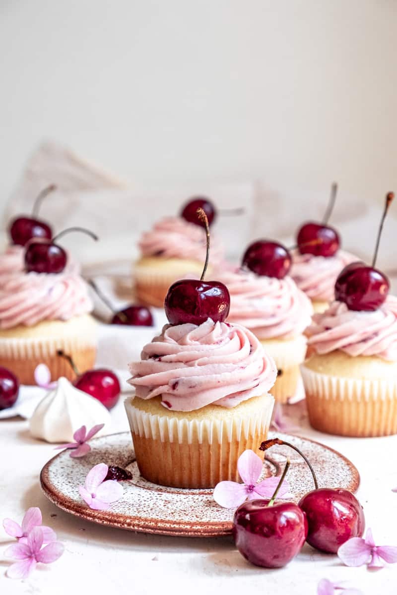 Cherry Cupcakes shown on a kitchen conter with fresh cherries and flowers.