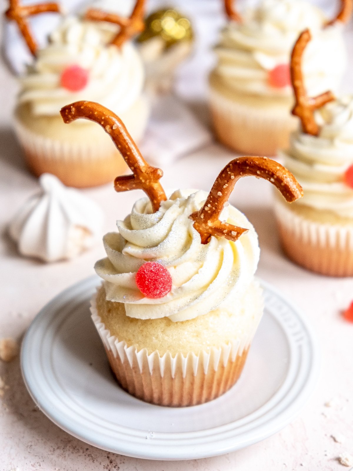 Vanilla reindeer cupcakes shown decorated, there are mini meringues and Christmas decorations in the background.