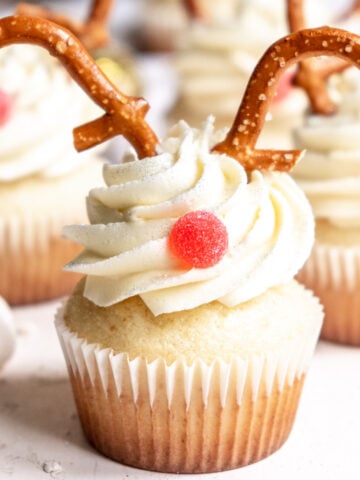 Reindeer cupcakes shown on a counter decorated with pretzels and a red jelly tot.