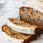 Banana bread with cream cheese frosting shown sliced on a plate