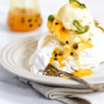Mango Pavlova on a plate with a fork and a jar of passionfruit puree in the background.