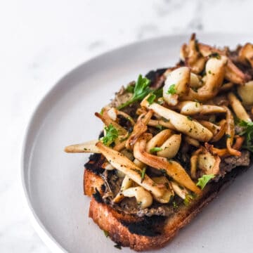 Mushroom Toast shown on a white plate on a marble kitchen counter.