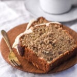 Image shows two slices of banana bread with cream cheese frosting on a small wooden plate.