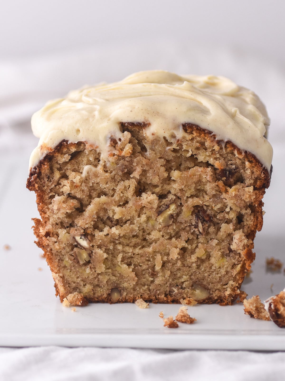 Image shows the banana bread loaf cut in half, you can see the moist banana cake studded with chunks of banana and chopped pecans.